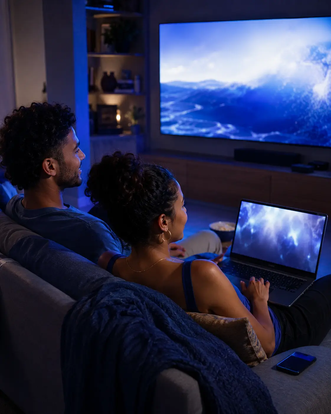 Casal assistindo televisão e usando notebook em casa